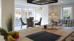 A modern kitchen with an induction cooktop, dining area with chairs, and a living room with a sofa. - Holiday apartment in Büsum with swimming pool (Büsum)