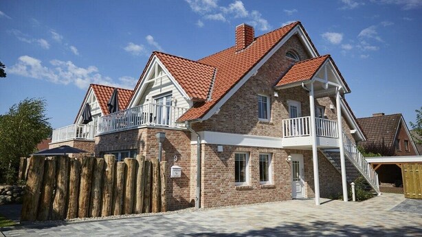 A two-story house with a brick exterior, a red-tiled roof, and a balcony on the upper floor. - Holiday apartment in Büsum with swimming pool (Büsum)