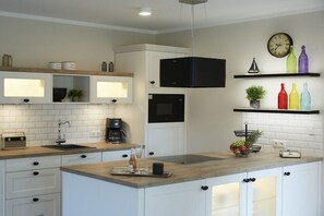 Een moderne keuken met witte kastjes, een houten aanrecht, een zwarte afzuigkap, een koffiezetapparaat en een klok aan de muur.