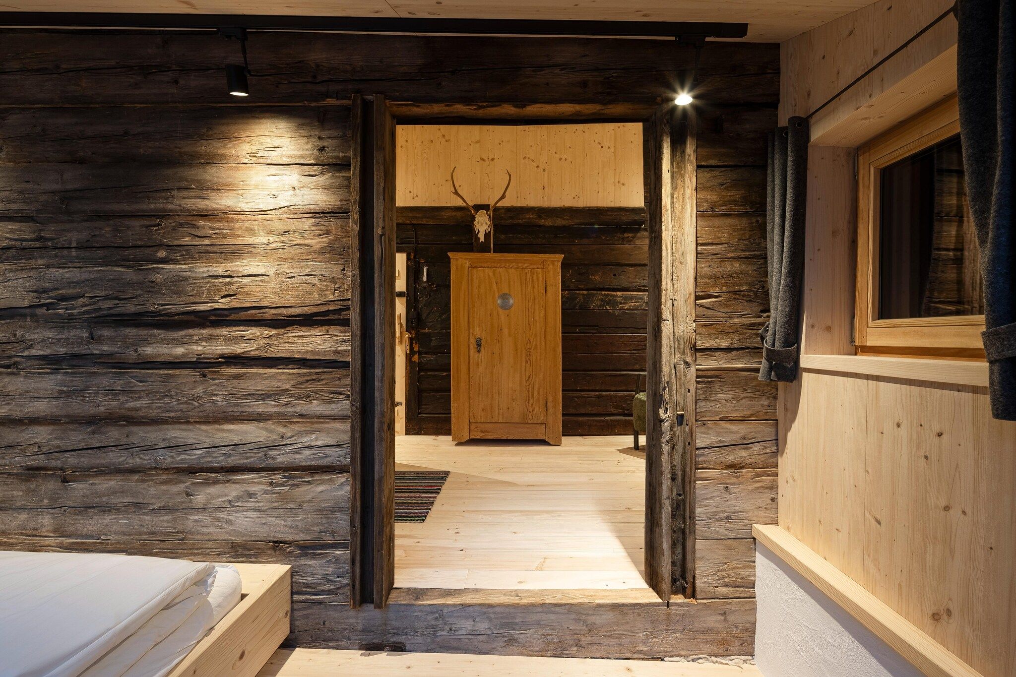 A wooden cabin interior with a central door, a window on the right, and a small step leading to a bedroom.