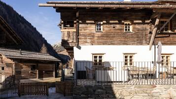 Un edificio tradicional de madera con base de piedra, un balcón y un patio amurallado.