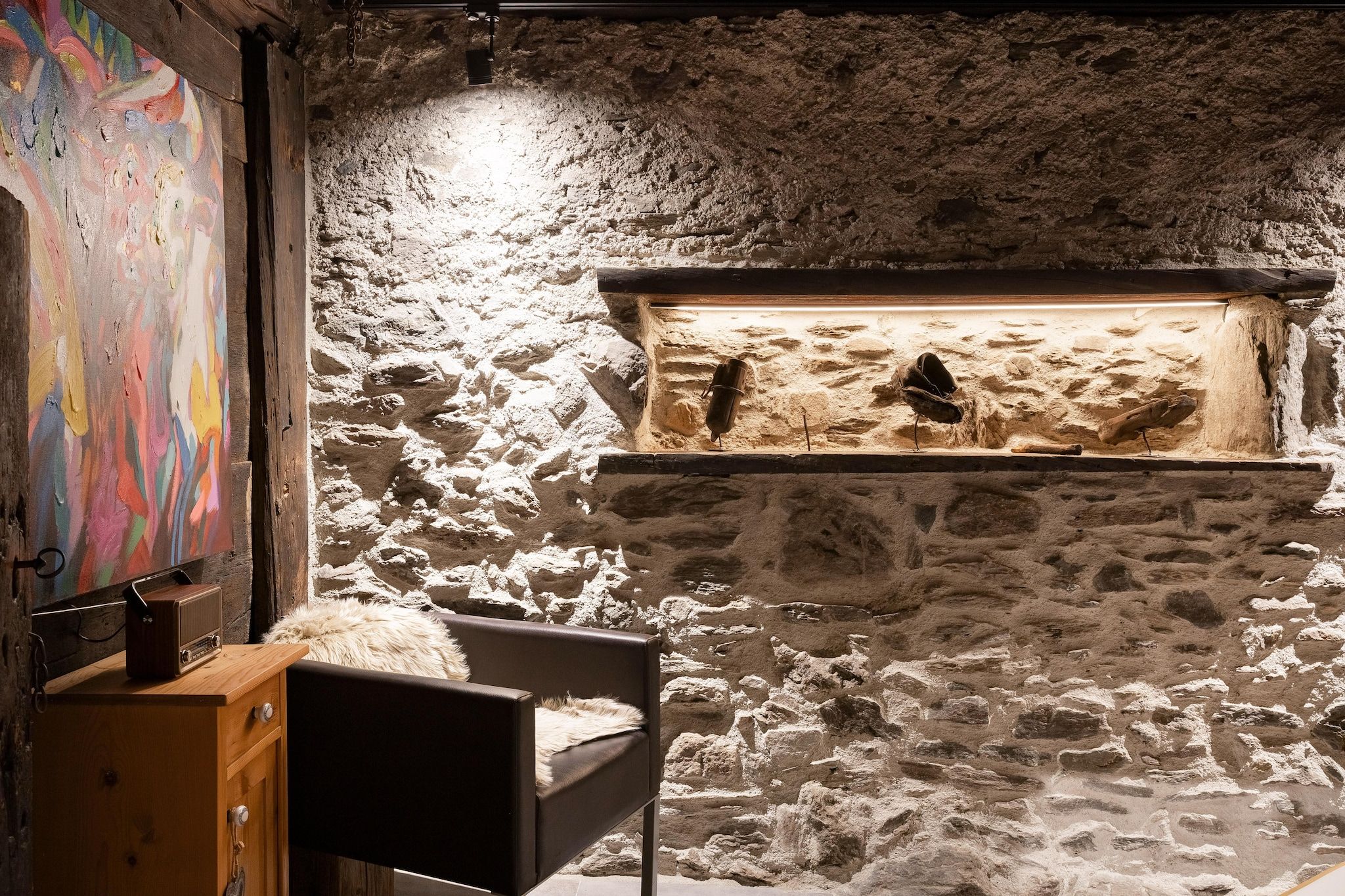 Una habitación con pared de piedra rústica, un armario de madera y una silla.