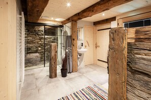 Une salle de bain moderne avec un mur en pierre, des poutres en bois, une douche en verre et un lavabo.