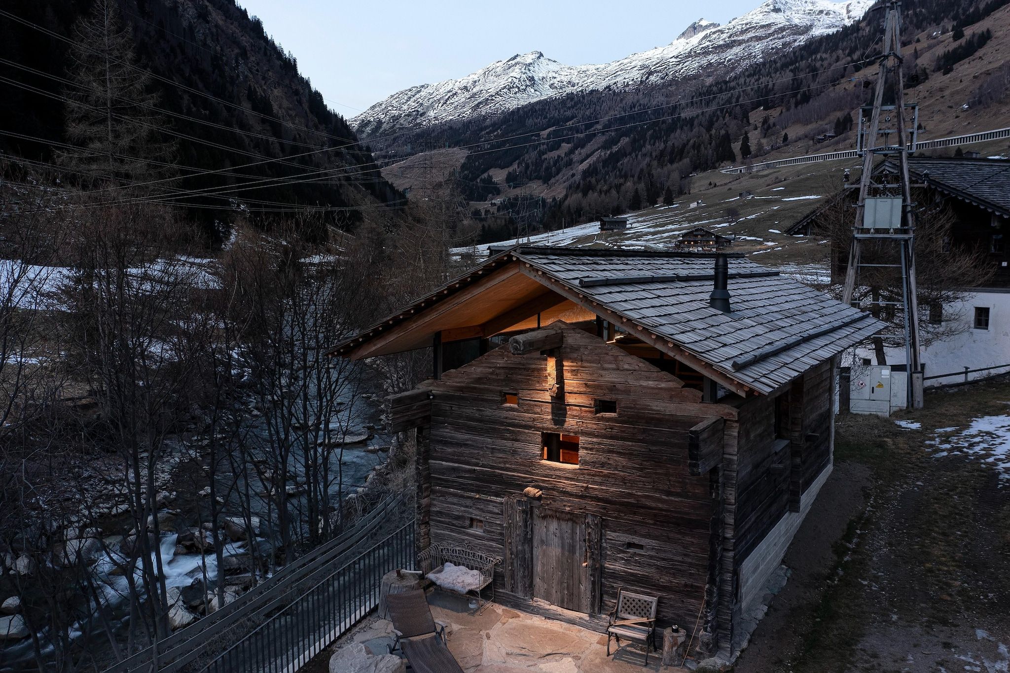Eine Holzhütte mit geneigtem Dach, umgeben von einer gebirgigen Landschaft.