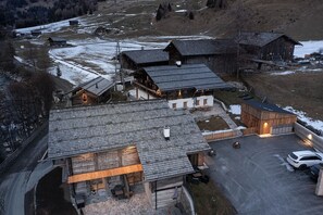 Un rústico refugio de montaña con varias construcciones de madera, un camino de piedra y un estacionamiento.