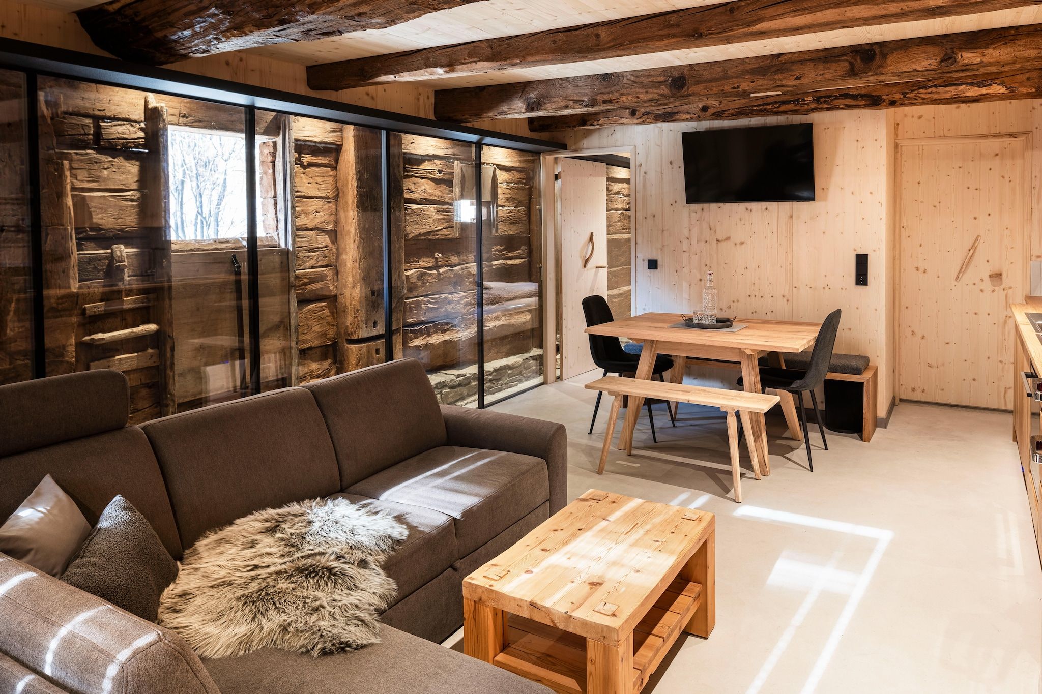 Un interior moderno con una mesa de comedor de madera, un sofá y un televisor montado en la pared.