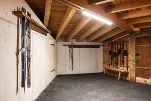 A ski storage room with wooden beams, a bench, and skis and ski poles on racks. - elegant apartment in a converted stable (Matrei in Osttirol)