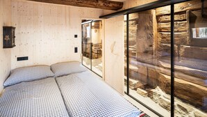Ein Zimmer mit einem Bett, Holzwänden und einer Glastrennwand mit Blick auf eine Steinstruktur.