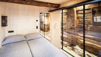 Una habitación con cama, paredes de madera y un separador de vidrio que ofrece vistas a una construcción de piedra.