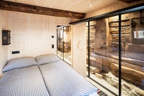 A room with a bed, wooden walls, and a glass partition with a view of a stone structure. - elegant apartment in a converted stable (Matrei in Osttirol)