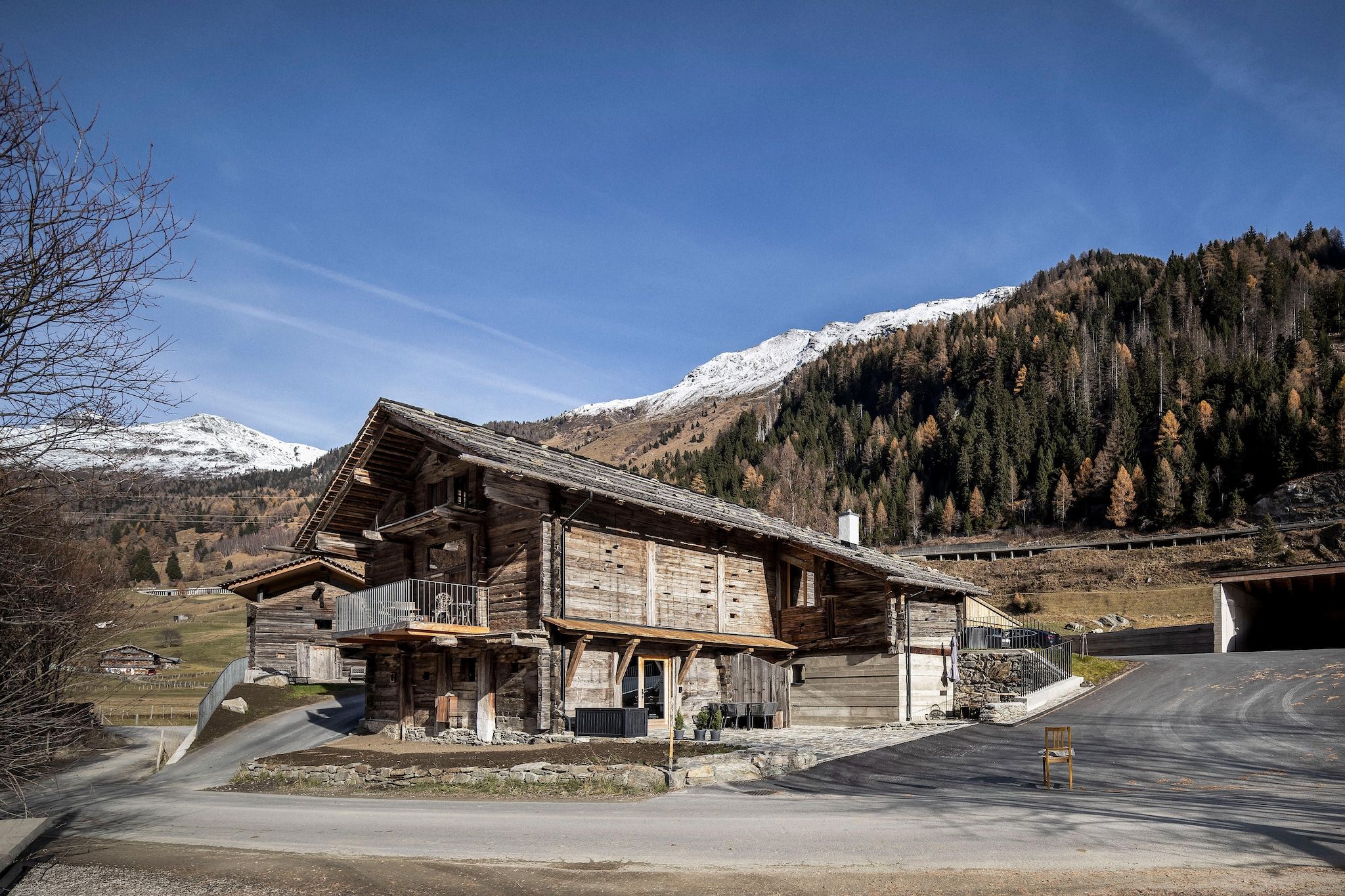 Ein rustikales Holzhaus mit Balkon vor einer Kulisse aus schneebedeckten Bergen und einem bewaldeten Hügelhang.