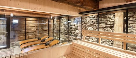 Sala de sauna com bancos de madeira e parede de pedra ao fundo.