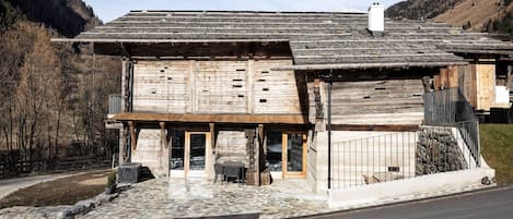 Un bâtiment rustique en bois, avec des fondations en pierre, un porche en bois et un portail en métal.