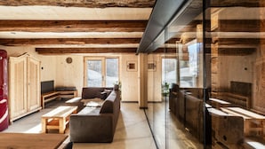 Ein geräumiger Raum mit Holzbalken, einer Couch, einem Tisch und einer Glastrennwand.