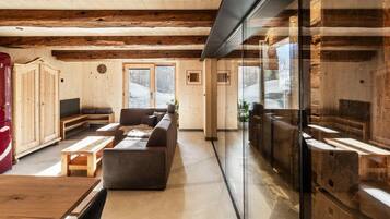 Una habitación amplia con vigas de madera, un sofá, una mesa y un separador de vidrio.