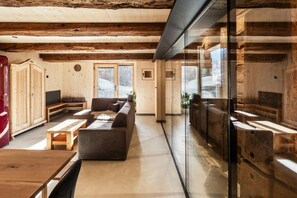 A spacious room with wooden beams, a sofa, a table, and a glass partition. - elegant apartment in a converted stable (Matrei in Osttirol)