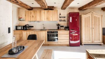 Una cocina con armarios de madera, un refrigerador rojo, una estufa y un comedor con mesa y sillas.