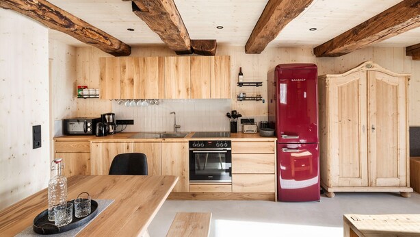 Eine Küche mit Holzschränken, einem roten Kühlschrank, einem Herd und einem Essbereich mit Tisch und Stühlen.