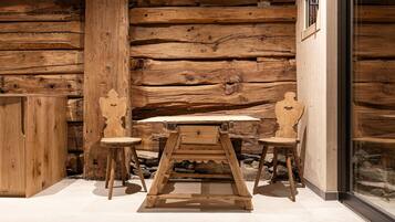 Interior rústico de madera con una mesa, dos sillas, un muro de piedra y una puerta de cristal.