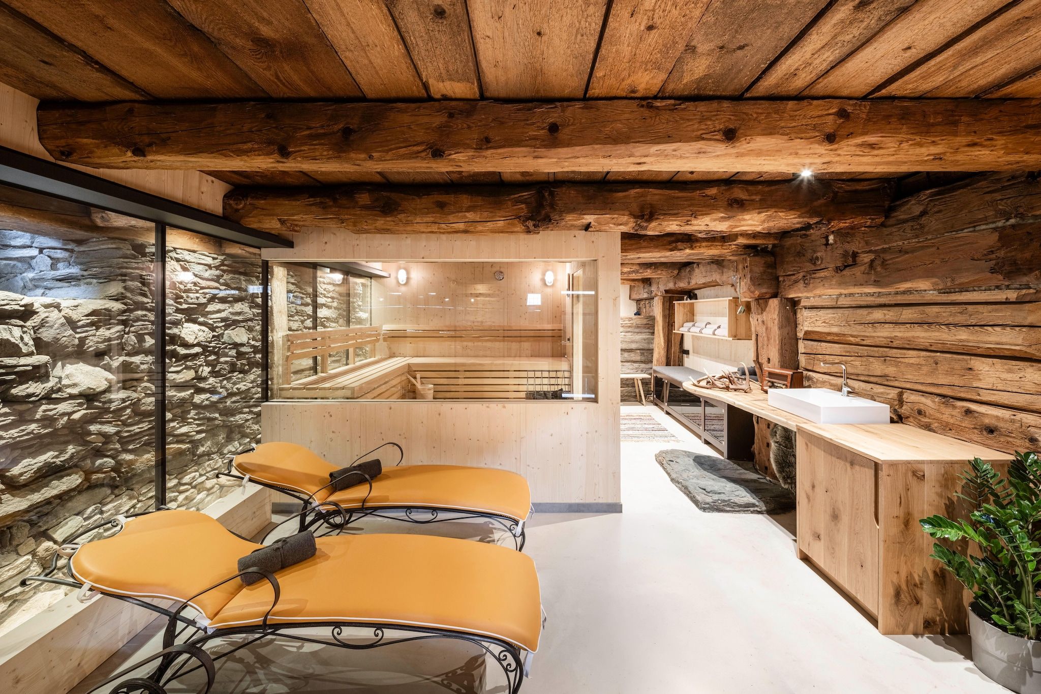 A spa room with wooden walls, a stone wall, a wooden bench, a massage table, and a sink.