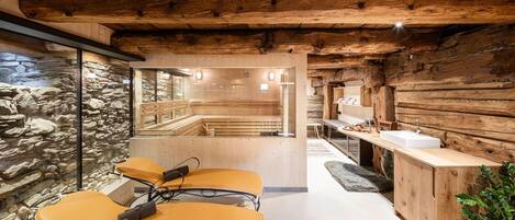 Un cuarto de spa con paredes de madera, una pared de piedra, un banco de madera, una camilla de masaje y un lavamanos.