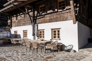 A rustic wooden building with a stone-paved patio and wicker furniture. - Charming chalet-style feeder house (Matrei in Osttirol)