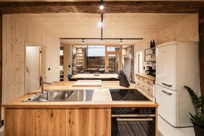 A modern kitchen with wooden cabinetry, a central island with a sink and stove, and a refrigerator.
