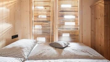 Une chambre à coucher avec un lit, une couette à carreaux, un oreiller et des stores en bois.