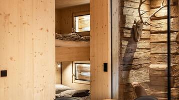 Un interior de madera con literas, una pared de piedra y una zona de comedor con sillas.