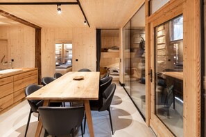 A modern interior with a wooden dining table, black chairs, and a kitchen area with a sink and cabinets. - Charming chalet-style feeder house (Matrei in Osttirol)