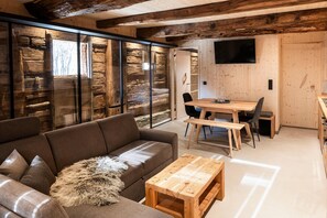 Um interior moderno com uma mesa de jantar de madeira, um sofá e uma televisão fixada na parede.