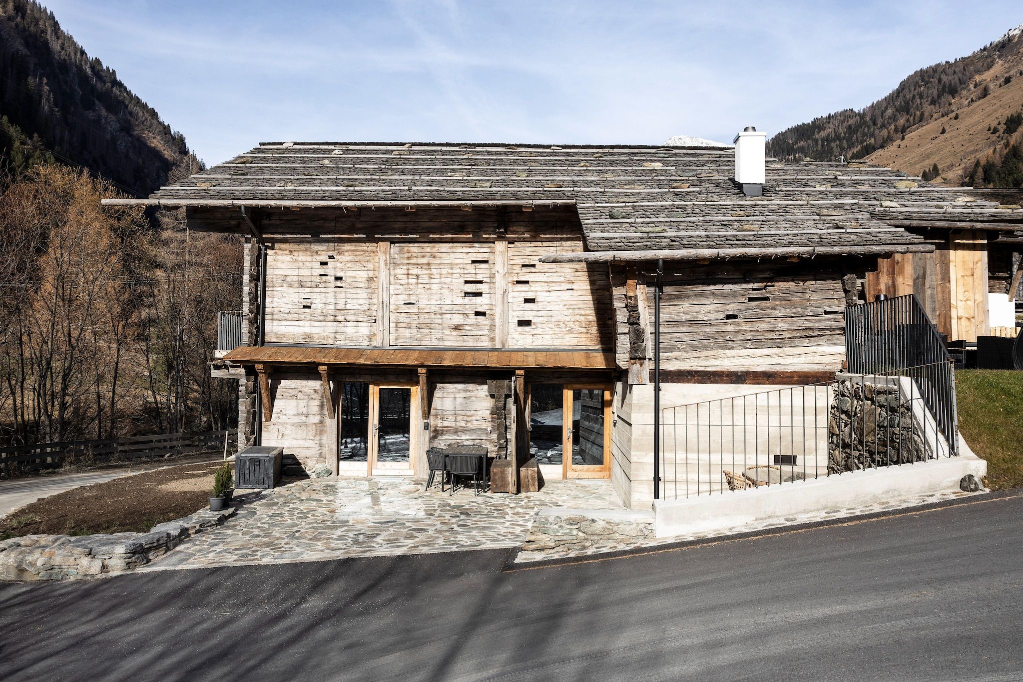 Ein rustikales Holzhaus mit steinernen Fundamenten, einer Holzveranda und einem Metalltor.