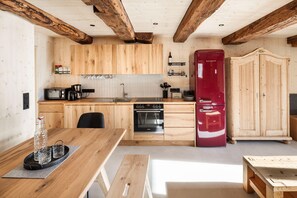Uma cozinha com armários de madeira, uma geladeira vermelha, um fogão e um espaço de refeições com uma mesa e cadeiras.