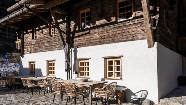 Ein rustikales Holzgebäude mit einer terrasse aus Natursteinplatten und Korbmöbeln.