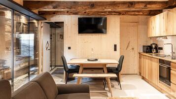 Ein modernes Interieur mit einem Holzesstisch, Stühlen, einer Couch, einer Küchenzeile und einem großen Fenster.