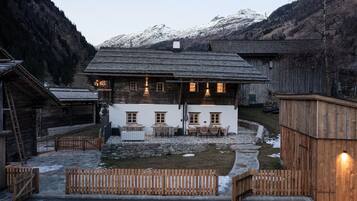 Un chalet rustique doté d’une terrasse en pierre, de clôtures en bois et d’un foyer extérieur.