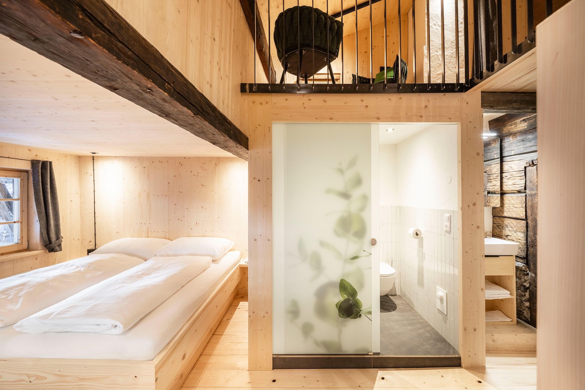 Ein Holzinnenraum mit einem Bett, einem Badezimmer und einer Treppe.