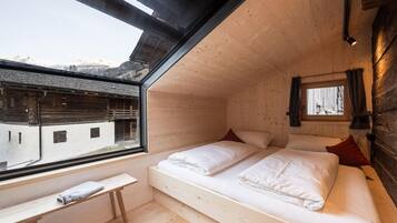 Une chambre avec un plafond en bois, un lit avec une literie blanche, une fenêtre donnant sur des immeubles et une petite table avec une serviette.