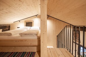 Interior de madeira com cama, escada e vista para o exterior.