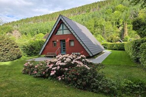A red cabin with a sloped roof, surrounded by lush greenery and a well-maintained lawn. - Holiday home with 1 bedroom (Simmerath)