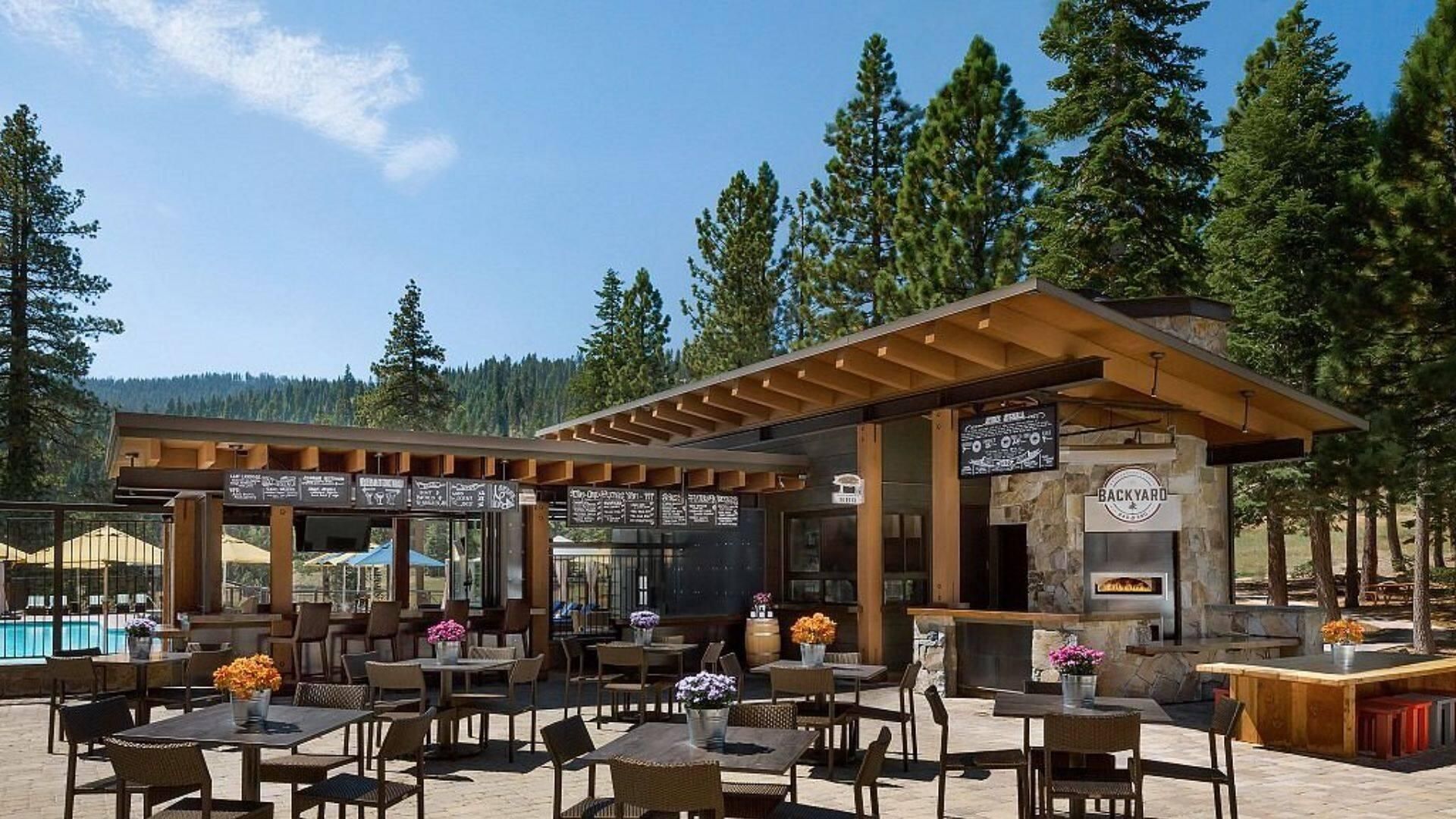 An outdoor seating area with tables and chairs, a pool, and a stone building labeled 'BACKYARD'.