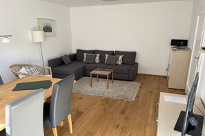 Ein modernes Wohnzimmer mit einer Couch, einem Couchtisch, einem Esstisch mit Stühlen, einer Lampe und einem Schrank.