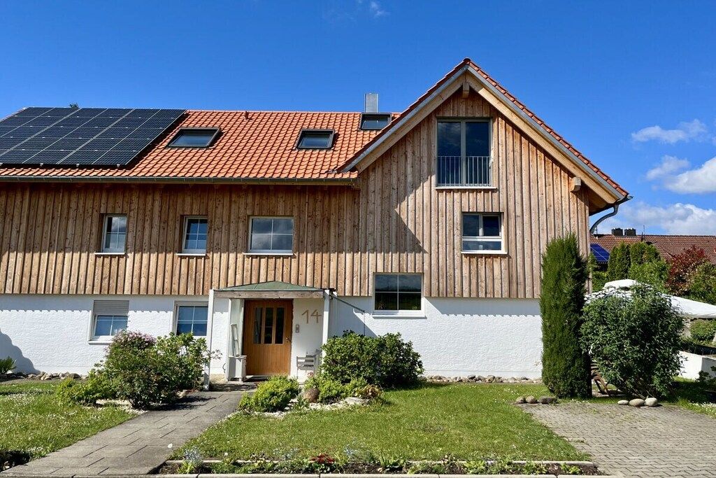 A two-story wooden house with a sloped roof, solar panels, and a small front porch.