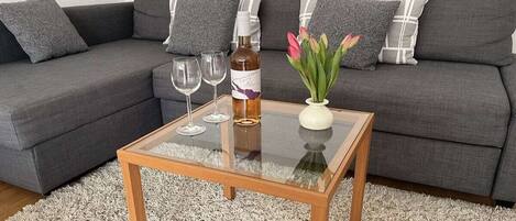 Una sala de estar moderna con un sofá gris, una mesa de centro de vidrio y un jarrón con flores.