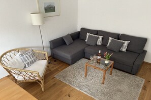 A living room with a grey sofa, a wicker chair, a small wooden coffee table, and a white lamp. - Holiday apartment in Stetten with barbecue (Stetten)