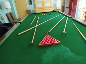 A pool table with cue sticks and balls, a chair, and a lamp.