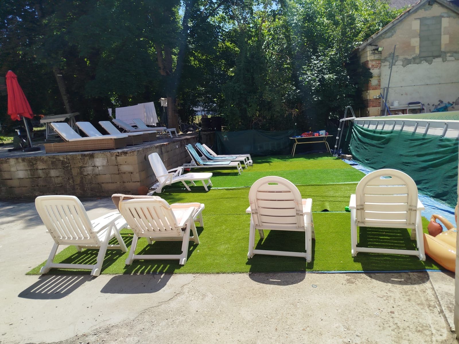 Ein Garten mit künstlichem Rasen, weißen Liegestühlen und einem Poolbereich.