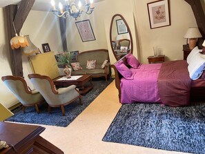 A bedroom with a bed, two chairs, a table, a mirror, and a chandelier.