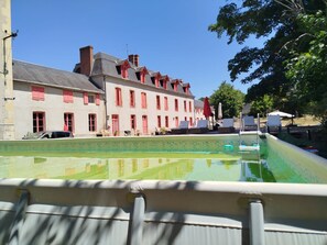 A swimming pool with a view of a row of buildings with red shutters and a clear sky. - 18TH-CENTURY CLAIREFONTAINE GARCHIZY CASTLE (Garchizy)