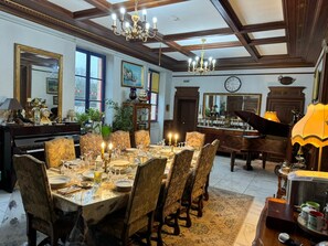 A dining room with a large table set for a meal, a piano, and a chandelier.